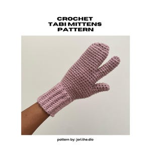 Op de afbeelding: Een close-up van een gehaakte roze tabi want. De want heeft een apart gedeelte voor de grote teen en is geribbeld bij de pols. De tekst "CROCHET TABI MITTENS PATTERN" staat bovenaan. De tekst "pattern by: jori.the.dio" staat onderaan.