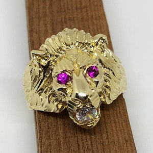 May include: A gold lion head ring with pink and clear gemstones for the eyes.