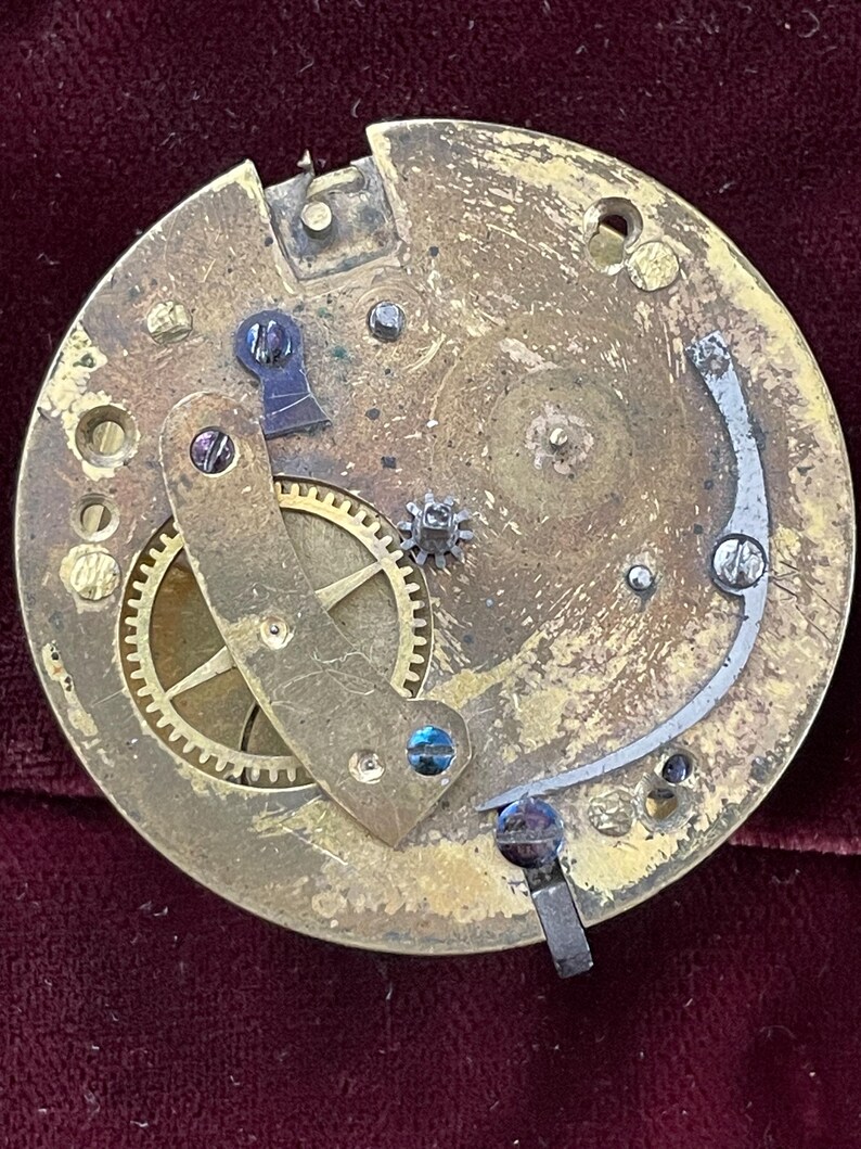 Op de afbeelding: Close-up van een messing uurwerk met tandwielen en een opwindslinger. Het uurwerk is gedemonteerd en toont de ingewikkelde werking van het horloge.