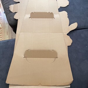 Op de afbeelding: Een kartonnen uitsparing van een cartoonfiguur, waarschijnlijk voor een promotionele display. De uitsparing is gevouwen en heeft twee gleuven om een ​​bord of andere promotionele materialen vast te houden.