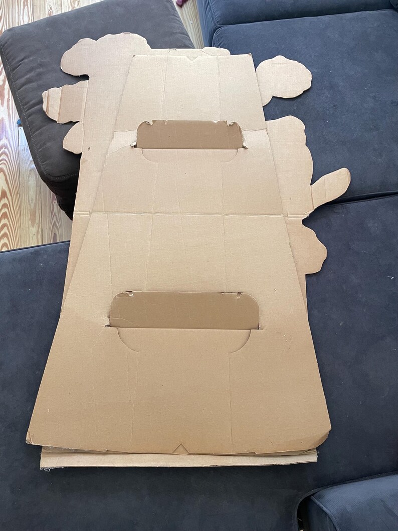 Op de afbeelding: Een kartonnen uitsparing van een cartoonfiguur, waarschijnlijk voor een promotionele display. De uitsparing is gevouwen en heeft twee gleuven om een ​​bord of andere promotionele materialen vast te houden.