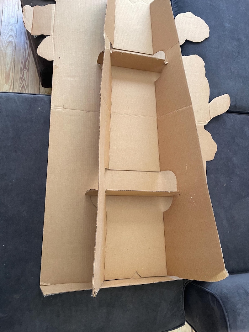Op de afbeelding: Een kartonnen doos met twee uitgesneden secties, waarschijnlijk voor het verpakken van een product. De doos is bruin en heeft een eenvoudig ontwerp.