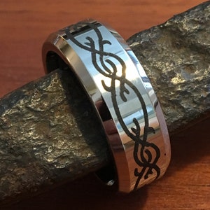 May include: A silver ring with a black, intricate design of a barbed wire pattern around the band.