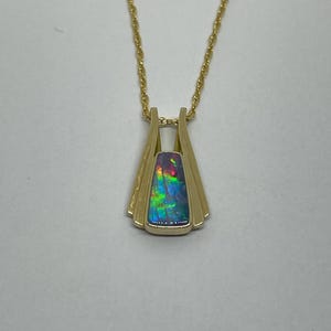 May include: A gold necklace with a pendant featuring a multi-colored opal stone set in a gold frame.