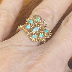 Op de afbeelding: Een gouden ring met een cluster van opaalstenen in de vorm van een vlinder.