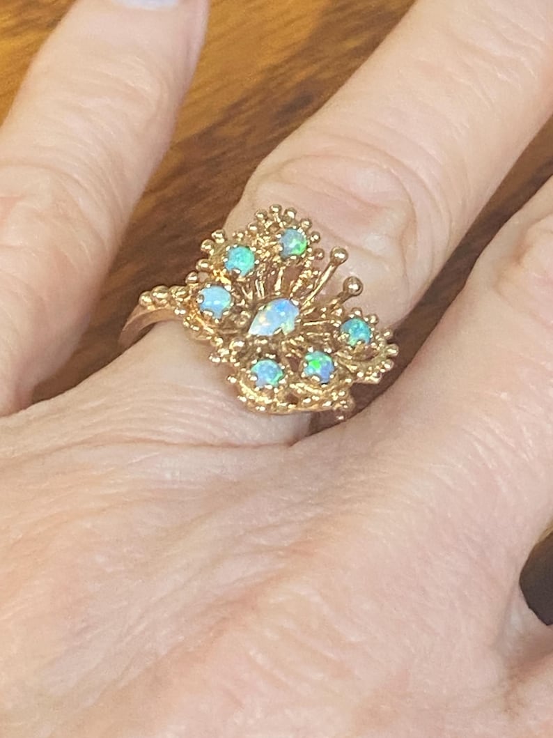 Op de afbeelding: Een gouden ring met een cluster van opaalstenen in de vorm van een vlinder.
