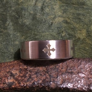 May include: A silver ring with a brushed finish and a gold cross design.