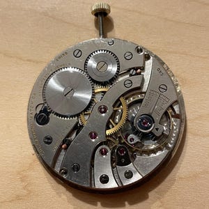 May include: Close-up of a silver watch movement with seventeen jewels, Swiss made, and the text "OK3" on the side.