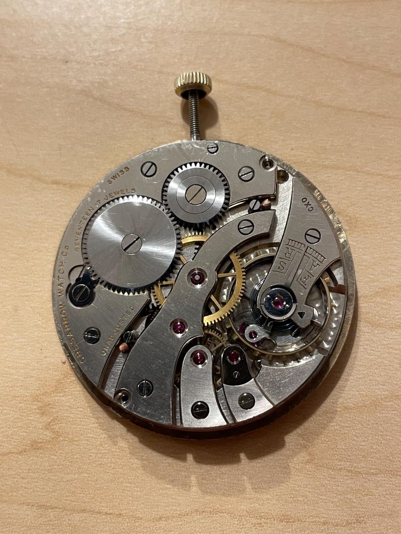 May include: Close-up of a silver watch movement with seventeen jewels, Swiss made, and the text "OK3" on the side.