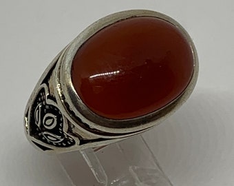 Op de afbeelding: Een zilveren ring met een ovale carneol steen. De ring heeft een ingewikkeld ontwerp rond de steen.