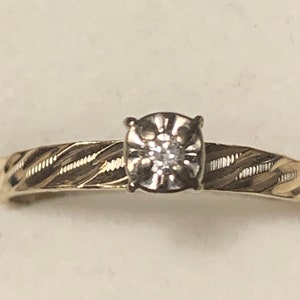 May include: A gold band ring with a diamond set in a prong setting. The band has a twisted design.