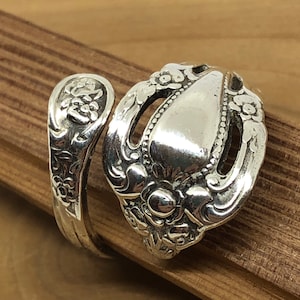 May include: A silver spoon ring with a floral design. The ring is made from a vintage spoon and is a unique piece of jewelry.