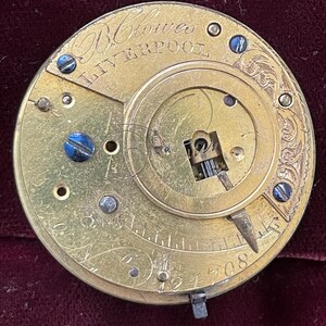 Op de afbeelding: Close-up van een goudkleurig zakhorlogemechanisme met de inscriptie "Blowes Liverpool" en het nummer "194708".
