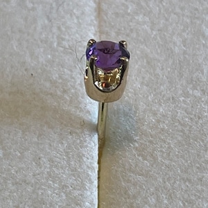 May include: A single amethyst stud earring with a gold setting. The earring is on a white background.