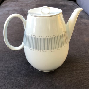 May include: White ceramic coffee pot with a silver lid and a geometric pattern of gray lines and circles around the body.