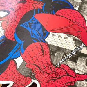 Op de afbeelding: Een rood en blauw Spiderman-actiefiguur met een web shooter in zijn hand, zwaaiend aan een weblijn tegen een stadsachtergrond.