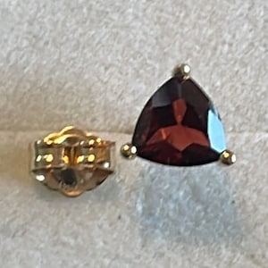 May include: A pair of gold earrings with a triangular red gemstone. The earrings have a post back closure.