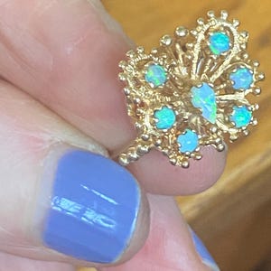 Op de afbeelding: Een gouden ring met een delicaat, ingewikkeld ontwerp met meerdere opaal edelstenen. De ring is bezet met een cluster van opalen in een bloemmotief.