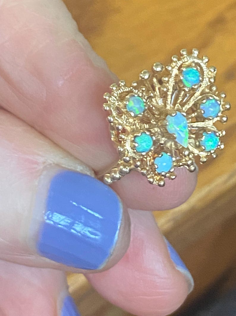 Op de afbeelding: Een gouden ring met een delicaat, ingewikkeld ontwerp met meerdere opaal edelstenen. De ring is bezet met een cluster van opalen in een bloemmotief.