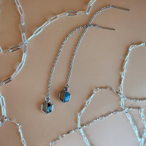 May include: Two silver chain necklaces with geometric pendant charms. The charms are hexagonal and have a blue and white stone inlay.
