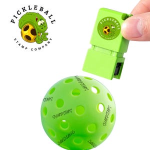 May include: A green pickleball with the word "SHARPSTARS" printed on it, and a green stamp with the text "PICKLEBALL STAMP COMPANY" and a cartoon pickleball character. The stamp is being held over the ball.
