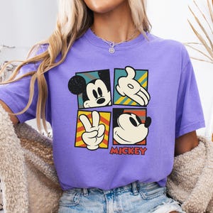 May include: Purple short-sleeved t-shirt with a vintage-style graphic of Mickey Mouse in four different poses. The graphic includes the text "MICKEY".