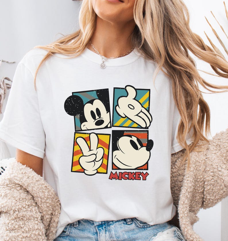 May include: White t-shirt with a vintage-style graphic of Mickey Mouse in four different poses. The graphic is in a colorful block design with yellow, red, blue, and green accents. The text "MICKEY" is printed below the graphic.