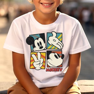 May include: White t-shirt with a colorful graphic of Mickey Mouse in four different poses. The graphic includes the text "MICKEY".