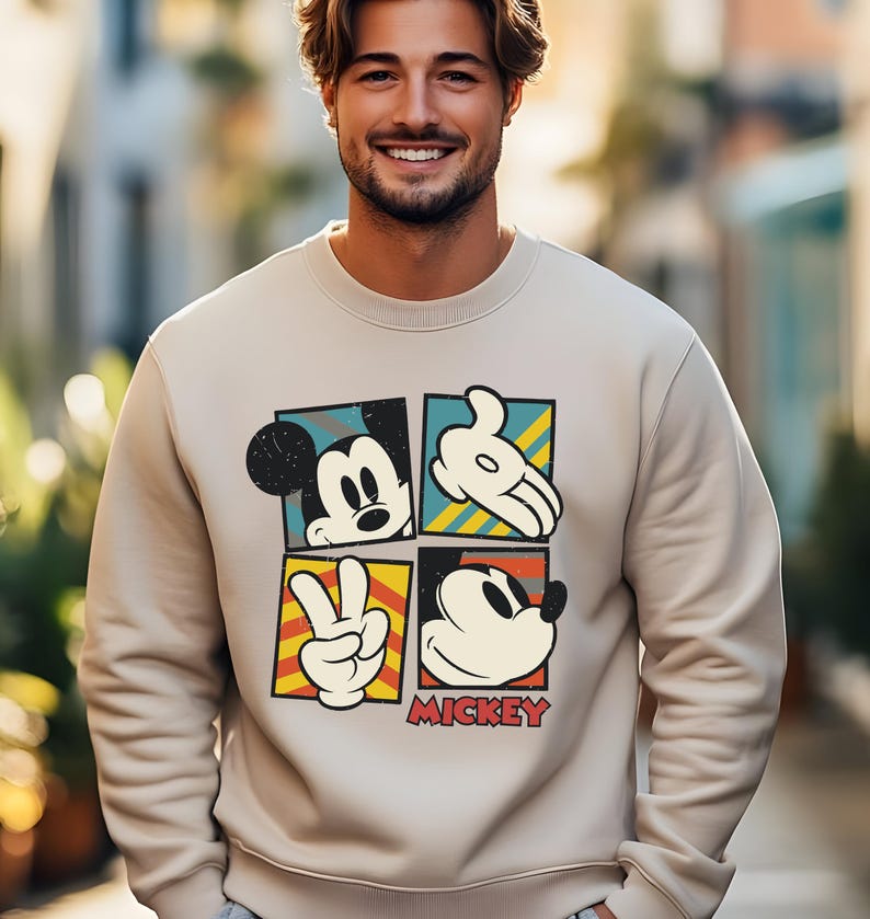 May include: A beige sweatshirt with a vintage-style graphic of Mickey Mouse in four different poses. The graphic is in a colorful block design with the word "MICKEY" printed below.