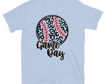 May include: Light blue t-shirt featuring a baseball design with a black and white leopard print baseball and red stitching. The words "Game Day" are written in black script below the baseball.