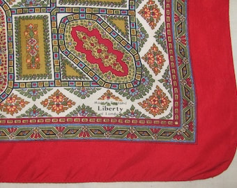 May include: A square scarf featuring a vibrant red border and a central pattern of intricate paisley and floral motifs in shades of gold, blue, and green. The fabric includes the printed text Made in England Liberty of London.