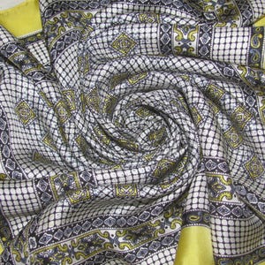 May include: A patterned silk scarf in white, black, and yellow, with a repeating geometric design. The scarf has a yellow border and is arranged in a spiral. The pattern includes squares, diamonds, and paisley shapes.