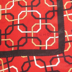 Peut inclure: Un foulard en soie rouge avec un motif géométrique d'octogones noirs, blancs et beiges entrelacés. Le foulard a une bordure noire et la marque "ECHO" est visible.