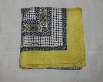 May include: A folded yellow silk pocket square with a patterned center. The center design features a white grid, paisley, and floral elements in navy, yellow, and light blue. The text "Made in England Liberty of London" is visible.