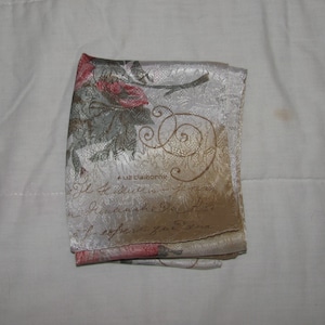 May include: A white silk scarf with a floral pattern and gold script. The script reads "Liz Claiborne" and "Il Aspetto"