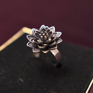 Puede incluir: Un anillo de plata con un dise&ntilde;o de flor de loto negra. El centro de la flor es de oro.