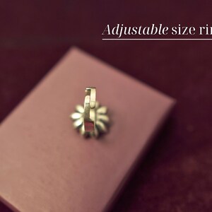 Puede incluir: Un anillo de tama&ntilde;o ajustable de oro en un expositor de terciopelo rosa. El anillo est&aacute; abierto por un lado y tiene un dise&ntilde;o decorativo.