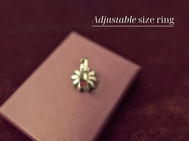 Puede incluir: Un anillo de tama&ntilde;o ajustable de oro en un expositor de terciopelo rosa. El anillo est&aacute; abierto por un lado y tiene un dise&ntilde;o decorativo.