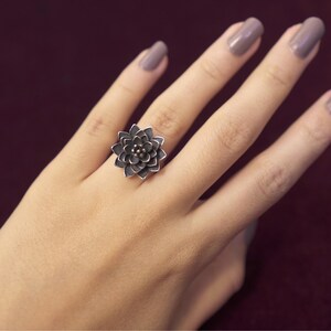 Puede incluir: Un anillo de plata con un dise&ntilde;o de flor. La flor est&aacute; hecha de m&uacute;ltiples capas de p&eacute;talos y tiene un peque&ntilde;o centro.