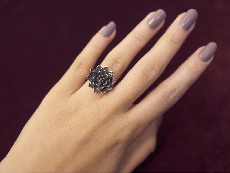 Puede incluir: Un anillo de plata con un dise&ntilde;o de flor. La flor est&aacute; hecha de m&uacute;ltiples capas de p&eacute;talos y tiene un peque&ntilde;o centro.