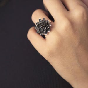 Puede incluir: Un anillo de plata con un dise&ntilde;o de flor negra.