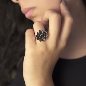 Puede incluir: Un anillo de plata con un dise&ntilde;o de flor detallado. La flor es de color gris oscuro y tiene un aspecto tridimensional.