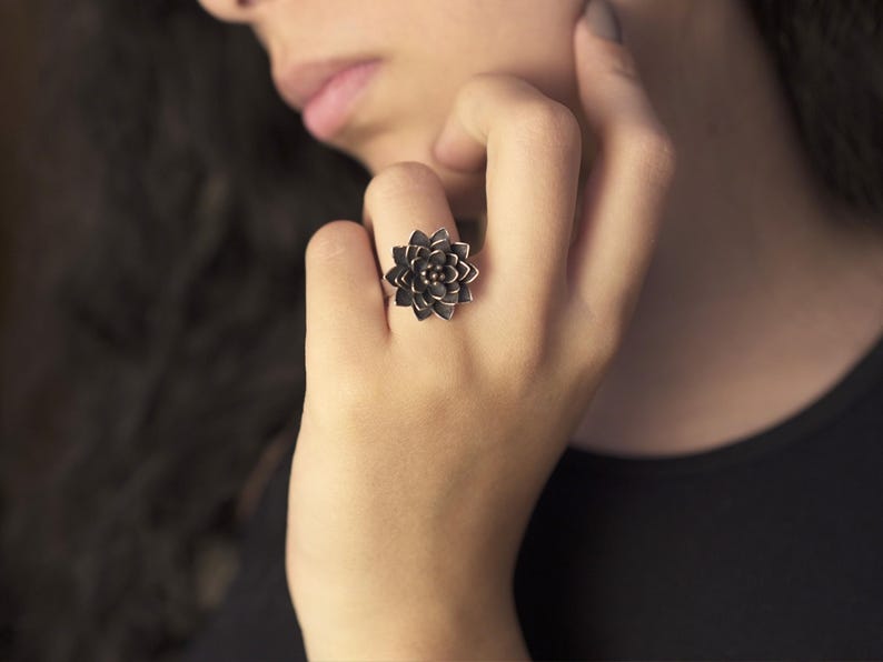 Puede incluir: Un anillo de plata con un dise&ntilde;o de flor detallado. La flor es de color gris oscuro y tiene un aspecto tridimensional.
