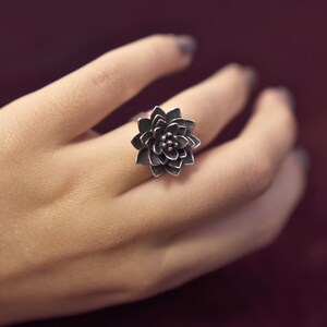 Puede incluir: Un anillo de plata con un dise&ntilde;o de flor detallado. El anillo se lleva en un dedo.