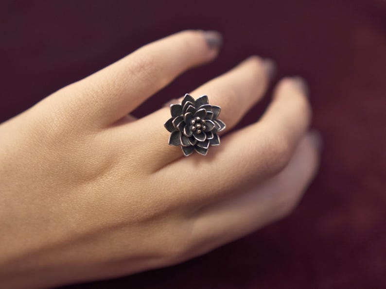 Puede incluir: Un anillo de plata con un dise&ntilde;o de flor detallado. El anillo se lleva en un dedo.