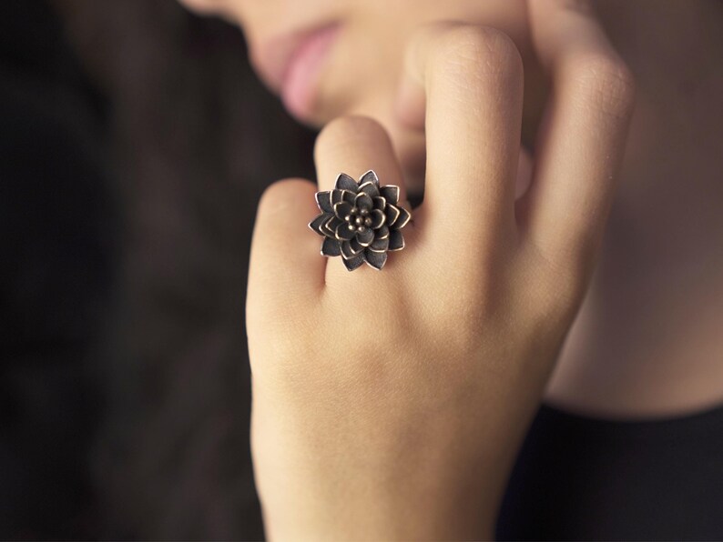 Puede incluir: Un anillo de plata con un dise&ntilde;o de flor negra.