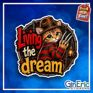 May include: A circular sticker featuring a brown tabby kitten wearing a brown fedora and a red and black striped sweater. The kitten has sharp metal claws on one paw. The text reads Living the dream in red and yellow. A small lantern hangs nearby.