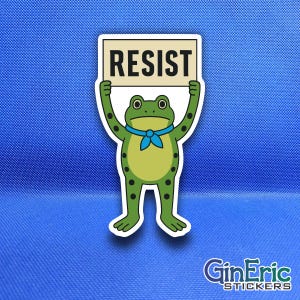 May include: A die-cut sticker featuring a green cartoon frog with a light green belly and black spots. The frog wears a blue neckerchief and holds a rectangular sign above its head with the word RESIST printed in bold black capital letters.