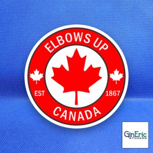May include: A circular sticker featuring a red and white design with a central maple leaf. The text reads ELBOWS UP, EST, 1867, and CANADA. Two smaller maple leaves are positioned on the left and right sides of the central emblem.
