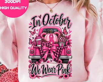 Könnte beinhalten: Ein hellrosa Sweatshirt mit einer Grafik eines rosa Pick-ups, der Kürbisse, einen Kaffeebecher und Blumen geladen hat. Das Design enthält Schmetterlinge, eine große Schleife und den Text In October We Wear Pink in schwarzer Schreibschrift.